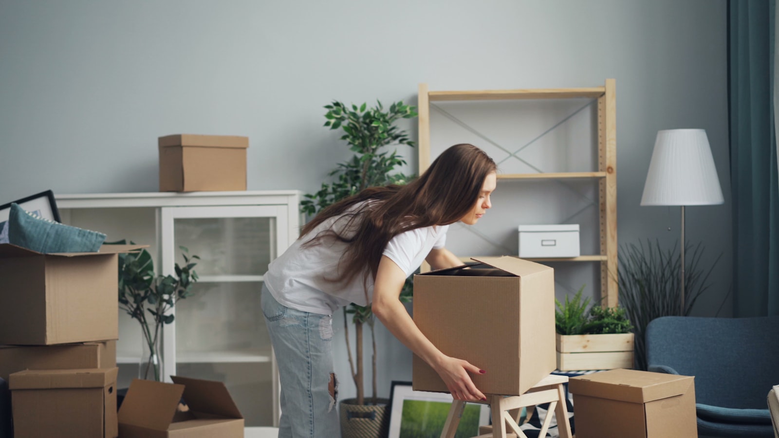 Woman carefully packing a cardboard box in a bright living room